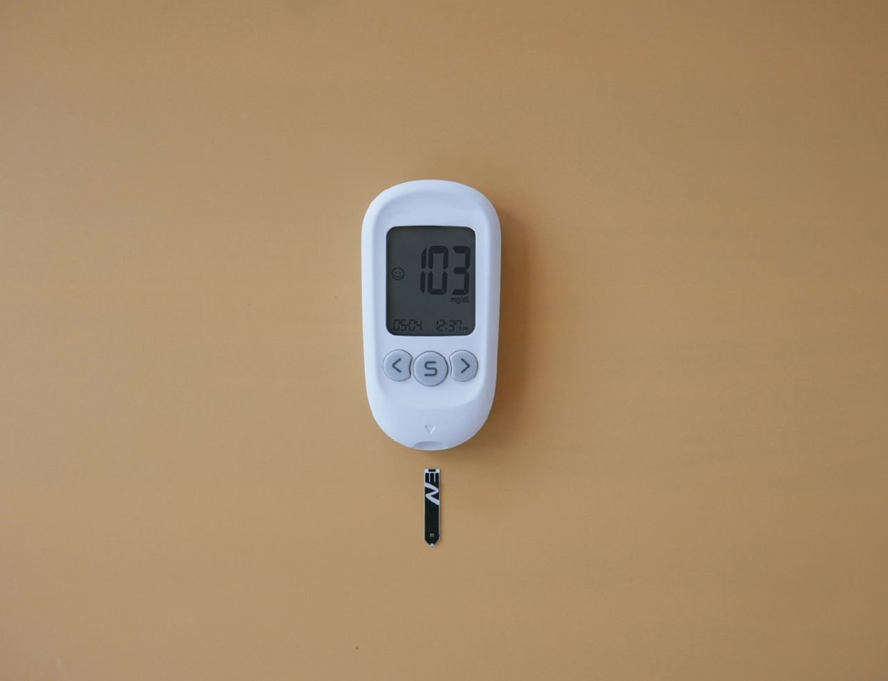 Close-up of a digital glucose meter displaying blood sugar level on a brown surface.