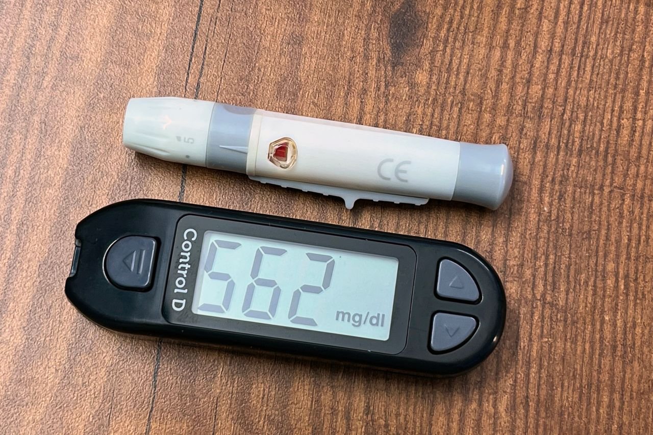 Glucometer showing 562 mg/dl indicating high blood sugar level on a wooden table.