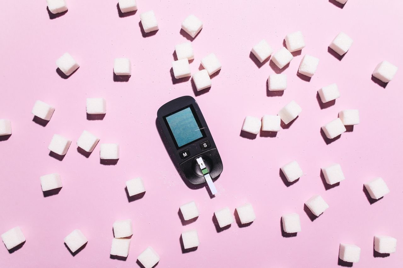Blood glucose meter surrounded by sugar cubes on a pink background, highlighting diabetes awareness.